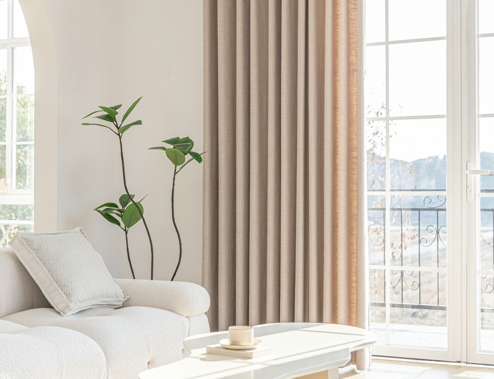 Clean living room with a white sofa, a plant, and light coming through tall windows